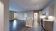 This well-designed single-floor residence offers a thoughtful layout with modern finishes and a cohesive neutral color palette throughout. The heart of the home is an open-concept kitchen and living area, where dark hardwood-style flooring flows seamlessly underfoot. The kitchen is equipped with stainless steel appliances, including a refrigerator, range, and microwave, complemented by granite countertops, two-tone cabinetry in white and wood-grain finishes, and a central island with a built-in sink. Track lighting illuminates the kitchen, adding both functionality and a contemporary touch. The spacious living area opens to the outdoors through a set of French doors with transom windows above, filling the space with natural light and offering outdoor views. The bedrooms are carpeted for comfort and feature windows with blinds that invite additional natural light. The bathroom is finished with a full tub-shower combination, wood-style flooring, and clean white fixtures. A connecting hallway links the kitchen to the rest of the home, providing a practical and organized flow. The overall ambiance is clean, modern, and move-in ready, with consistent neutral tones creating a calm and inviting atmosphere throughout.