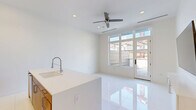 This modern 1-bedroom, 1-bathroom unit in Birmingham, MI offers a thoughtfully designed open-concept layout with clean, contemporary finishes throughout. The main living area seamlessly integrates the kitchen and living space, anchored by gleaming large-format white tile flooring that reflects abundant natural light. The kitchen features a striking island with a quartz countertop, an undermount sink with a professional-style pull-down faucet, warm wood cabinetry, and stainless steel appliances including a refrigerator, microwave, and range. A ceiling fan overhead and recessed lighting add comfort and functionality. Large windows and a glass door open to an outdoor area, flooding the space with natural light and providing a connection to the exterior. The living area includes a wall-mounted media console and ample room for furnishings. The bedroom is distinguished by a bold herringbone-patterned accent wall, vibrant blue cabinetry above, and the same elegant tile flooring, creating a stylish and unique retreat. The bathroom is finished in crisp white tile and features a glass-enclosed walk-in shower with a built-in bench and polished chrome hardware. A dedicated closet and hallway complete this efficiently designed, move-in-ready unit.