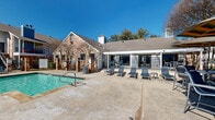 Located at Sierra Springs in Bedford, Texas, this outdoor pool area — designated as Pool 2 — is a well-appointed community amenity designed for relaxation and recreation. The centerpiece is a generously sized swimming pool with clearly marked depth indicators, offering clear, blue-green water surrounded by a broad concrete sundeck. Multiple sling-style lounge chairs are arranged along the poolside, providing ample space for sunbathing under the Texas sky.

Adjacent to the pool, a covered patio area features a striped canopy structure that offers shaded seating, making it a comfortable retreat during warmer days. A separate outdoor lounge space includes high-top tables and chairs positioned near raised stone planters with low-maintenance landscaping, adding a refined touch to the environment.

The pool area is enclosed by a classic brick-and-iron perimeter fence with gated entry points framed by decorative brick columns. The surrounding architecture reflects traditional brick construction with pitched, shingled rooflines consistent with the broader community aesthetic. Mature trees dot the landscape, providing natural shade and a sense of established character. The open layout and clear sight lines throughout the space create an inviting, community-focused atmosphere ideal for both active use and quiet relaxation.