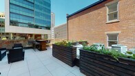 Situated in the heart of downtown Columbus, Ohio, this single-floor property at 43 W Long St offers a compelling blend of urban character and functional design. The most distinctive feature of the space is its expansive outdoor terrace, which provides an open-air retreat amid the city's skyline. The terrace is appointed with large, dark-stained wood raised planter boxes filled with lush greenery, adding a natural contrast to the surrounding urban environment. A bar area with high-top seating makes the terrace well-suited for entertaining or casual gatherings, while the classic brick exterior wall lends a sense of historic character to the setting. The terrace's light-toned tile flooring complements the clean lines of the outdoor layout, and the backdrop of neighboring glass high-rises reinforces the property's prime downtown location. The interior spaces, while more dimly lit in available imagery, feature windowed rooms with natural light filtered through blinds, suggesting practical and adaptable interior areas. Overall, the property combines the charm of brick architecture with modern outdoor amenities, making it a versatile space in one of Columbus's most central and accessible urban corridors.