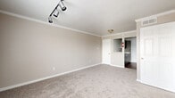 Located at 15570 Bellaire Blvd in Houston, TX, this two-bedroom, one-bathroom unit offers a practical and well-appointed single-floor layout. The living area features soft carpet flooring, neutral beige walls, and elegant crown molding, with adjustable track lighting that provides focused illumination throughout. A large window near the front entry allows natural light to fill the space while offering views of the surrounding neighborhood. The spacious primary bedroom continues the carpeted flooring and crown molding detail, with additional track lighting and ample room for furnishings. The second bedroom also features carpet, a ceiling fan, and a bright window with exterior views, making it suitable as a bedroom or home office. Four closets throughout the unit provide generous storage options. The galley-style kitchen is equipped with gray cabinetry, light stone-look countertops, a stainless steel sink, a dishwasher, a range, and a full-size refrigerator, all set atop rich wood-look vinyl flooring. The full bathroom includes a tub-shower combination, a white vanity with stone-look countertop, a mirrored medicine cabinet, and matching wood-look flooring, creating a clean and cohesive aesthetic.