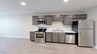 Located at 128 Bass Pro Dr in Sevierville, Tennessee, this single-floor, one-bedroom, one-bathroom unit offers a well-organized and functional layout. The kitchen serves as a central feature of the space, showcasing dark-toned cabinetry with ample upper and lower storage, white countertops, and a full suite of stainless steel appliances including an electric range, microwave, dishwasher, and refrigerator. Recessed lighting illuminates the kitchen, which flows naturally into the hallway and living areas via light hardwood-style flooring that runs throughout the main spaces. The bedroom is finished with soft wall-to-wall carpeting in a neutral tone, a window dressed with horizontal blinds that allows natural light to enter, and a built-in closet with a bifold door. The bathroom features matching dark wood cabinetry with a vanity sink, a lighted mirror, light hardwood-style flooring, and an open closet area with a hanging rod for additional storage. Neutral beige walls throughout the unit create a clean, cohesive aesthetic. The overall design emphasizes practicality and comfort, making this a straightforward and well-appointed living space in the heart of Sevierville.