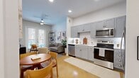 This well-designed one-bedroom, one-bathroom unit maximizes its compact footprint through an open-plan layout that seamlessly integrates the kitchen, dining, and living areas. Polished concrete floors in a warm amber tone flow consistently throughout, lending a cohesive, modern aesthetic.

The kitchen features gray shaker-style cabinetry extending to the ceiling, white subway tile backsplash, light countertops, and a full suite of stainless steel appliances, including a range, microwave, dishwasher, and refrigerator. A round dining table sits adjacent, comfortably accommodating intimate gatherings.

The living area is brightened by large French doors that invite natural light and provide outdoor access. A ceiling fan, recessed lighting, and elevated ceilings contribute to an airy feel. The bedroom offers a dedicated closet, a sizable window with exterior views, and the same warm concrete flooring.

The bathroom maintains the unit's consistent design language with gray cabinetry, a white tiled shower, and polished concrete floors. Overall, the space presents a clean, contemporary ambiance with efficient, thoughtfully arranged interiors throughout.