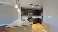 This thoughtfully designed single-floor residence offers a cohesive blend of modern aesthetics and functional living. The open-concept layout connects the kitchen and living area seamlessly, creating an inviting and spacious atmosphere.

The kitchen is a standout feature, showcasing dark espresso cabinetry that extends to the ceiling, a classic white subway tile backsplash, and a full suite of stainless steel appliances including a range, microwave, and refrigerator. A generous granite-topped island with an undermount sink serves as both a prep space and a natural gathering point, illuminated by elegant pendant lights hanging above. Track lighting overhead ensures the workspace is always well-lit.

The living area flows naturally from the kitchen, featuring warm hardwood-style flooring and a tray ceiling detail that adds architectural dimension. Natural light streams in through blinds-fitted windows, enhancing the open feel of the space.

The bedrooms offer a comfortable retreat; one features rich hardwood-style flooring and a ceiling fan, while the other is finished with plush carpeting, both receiving natural light from windows with blinds.

The bathroom is finished with large-format neutral tile flooring and tub surround, a dark vanity topped with granite, and a well-framed mirror, delivering a clean and polished look throughout.