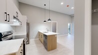 This contemporary single-floor unit offers a well-designed layout with 3 bedrooms and 3 bathrooms, thoughtfully arranged to maximize functionality and comfort. The open-concept kitchen serves as the heart of the home, showcasing warm wood-grain cabinetry, crisp white countertops, a central island with an undermount sink, stainless steel appliances, and stylish black pendant lighting. Notably high ceilings amplify the sense of space throughout the main living and kitchen area, which flows seamlessly into the living room, complete with a wall-mounted mini-split heating and cooling unit. Light-toned laminate flooring runs throughout, lending a clean, cohesive aesthetic. The bedrooms are bright and airy, each benefiting from large windows that frame sweeping views of the surrounding cityscape and distant mountain ranges. The primary bedroom includes a dedicated closet area. Each of the three bathrooms features consistent warm wood vanity cabinetry with black hardware and white countertops, with at least one full bathroom offering a soaker tub and shower combo. A dedicated laundry area houses a stacked washer and dryer unit for added convenience. Neutral grey tones throughout the walls complement the modern finishes, creating a calm and inviting atmosphere.