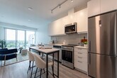 Located at 211 Queen St in Newmarket, Ontario, this one-bedroom, one-bathroom unit offers a thoughtfully designed open-concept layout with modern finishes throughout. Light oak-toned laminate flooring runs seamlessly across the entire space, complemented by bright white walls that enhance the sense of openness.

The kitchen is sleek and well-appointed, featuring flat-panel white cabinetry extending to the ceiling, a marble-look quartz countertop, a subway tile backsplash in a soft grey tone, and a full suite of stainless steel appliances including a refrigerator, electric range, built-in microwave, and dishwasher. A compact island with bar seating provides a practical dining and workspace.

The living area benefits from floor-to-ceiling sliding glass doors that open to a balcony, flooding the space with natural light and offering open views of the surrounding Newmarket skyline and treetops.

The bedroom is a calm and functional retreat, featuring a large sliding-door closet and its own floor-to-ceiling window with balcony access and outdoor views. The bathroom is finished with full-height grey rectangular wall tiles surrounding a soaker tub and shower combination, paired with clean white fixtures and chrome hardware.