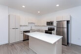 This well-designed 2-bedroom, 2-bathroom residence in West Valley City, Utah offers a thoughtfully planned single-floor layout with clean, modern aesthetics throughout. The open-concept living and kitchen area serves as the heart of the home, featuring light wood-look flooring, recessed lighting, and bright white walls that create a fresh, airy atmosphere. The kitchen is equipped with stainless steel appliances — including a refrigerator, range, microwave, and dishwasher — complemented by white flat-panel cabinetry, light countertops, and a central island that provides additional prep space and a natural gathering point. The living area flows seamlessly from the kitchen, offering a comfortable, open feel with natural light from a window fitted with blinds. Both bedrooms feature plush carpeting, windows with natural light, and clean white walls, with the primary bedroom offering a generous footprint. The two bathrooms are finished in a consistent modern style, with light wood-look flooring, white vanities with integrated sinks, and black hardware accents. One bathroom includes a tub-shower combination, while the other features a walk-in shower area. A dedicated closet adds practical storage. The overall design is cohesive, minimal, and move-in ready.