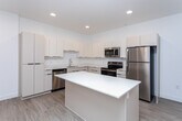 This well-designed 2-bedroom, 2-bathroom residence in West Valley City, Utah offers a thoughtfully planned single-floor layout with clean, modern aesthetics throughout. The open-concept living and kitchen area serves as the heart of the home, featuring light wood-look flooring, recessed lighting, and bright white walls that create a fresh, airy atmosphere. The kitchen is equipped with stainless steel appliances — including a refrigerator, range, microwave, and dishwasher — complemented by white flat-panel cabinetry, light countertops, and a central island that provides additional prep space and a natural gathering point. The living area flows seamlessly from the kitchen, offering a comfortable, open feel with natural light from a window fitted with blinds. Both bedrooms feature plush carpeting, windows with natural light, and clean white walls, with the primary bedroom offering a generous footprint. The two bathrooms are finished in a consistent modern style, with light wood-look flooring, white vanities with integrated sinks, and black hardware accents. One bathroom includes a tub-shower combination, while the other features a walk-in shower area. A dedicated closet adds practical storage. The overall design is cohesive, minimal, and move-in ready.