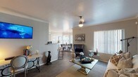 Located at 5151 E Guadalupe Rd in Phoenix, AZ, this single-story home offers a well-designed layout with a comfortable flow throughout. The living room features crown molding, wood-style flooring, and a ceiling fan, creating a welcoming and functional gathering space. Large windows with vertical blinds allow natural light to fill the room, while a dedicated seating area provides ample space for relaxing or entertaining.

The dining area is situated adjacent to the living room and benefits from a bay-style window configuration with a pendant light overhead, offering a bright and defined space for meals. It also provides direct access to an outdoor patio via a sliding glass door.

The galley-style kitchen is equipped with stainless steel appliances, including a refrigerator, range, and microwave, complemented by white cabinetry and light countertops. A dedicated in-unit laundry area with a stacked washer and dryer is conveniently accessible from the kitchen.

The primary bedroom includes a ceiling fan, carpeted flooring, wall-mounted shelving, and a sliding glass door leading to an outdoor patio. The bathroom features a wide vanity with a large mirror and ample storage. A secondary bedroom offers generous space with carpeted flooring and a large window for natural light.