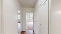 Located at 2900 Glenn Ave in Los Angeles, CA 90023, this single-story unit offers two bedrooms and two bathrooms within a compact, efficiently designed floor plan. The layout is connected by a central hallway lined with tall, built-in white cabinetry that provides generous storage and a clean, organized aesthetic. Flooring throughout the common areas consists of warm-toned hardwood, while both bedrooms feature plush wall-to-wall carpeting for added comfort. The primary bedroom is notably spacious, featuring a ceiling fan, a large window with views of surrounding greenery, and a distinctive blue accent wall that adds a touch of character. The second bedroom is bright and airy, with its own window allowing natural light to filter through. The kitchen is well-appointed with white cabinetry, granite-look countertops, a gas range, and a sink — all laid out in an efficient configuration over hardwood flooring. A dedicated closet adds further storage to the unit. Throughout the space, white walls and natural light create a clean, open ambiance. Windows in multiple rooms frame views of mature trees outside, contributing to a calm and inviting atmosphere throughout.