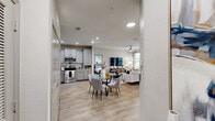 Located at 7116 Finn Hall Avenue in Charlotte, NC, this single-story, 2-bedroom, 2-bathroom home offers a thoughtfully designed open-concept layout. The combined living, dining, and kitchen area forms the heart of the home, finished with light wood-style flooring that flows seamlessly throughout. The kitchen is equipped with gray shaker-style cabinetry, granite countertops, a classic white subway tile backsplash, stainless steel appliances, and a deep undermount sink — a functional and visually appealing space. The dining area sits adjacent to the kitchen, while the living room benefits from large windows that invite abundant natural light and views of the surrounding greenery, complemented by a ceiling fan overhead. The spacious primary bedroom features a bold accent wall, ceiling fan, and generous natural light, accompanied by a private en-suite bathroom with granite vanity and a walk-in closet. The second bedroom also offers dual windows, a ceiling fan, and its own access to a full bathroom complete with a soaking tub and granite vanity. Additional spaces include a laundry room, utility room, and two closets. The home also features a covered outdoor area visible from the doll-house view, adding to its appeal.