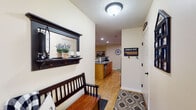 This single-floor home offers a thoughtfully designed layout that balances comfort and functionality throughout. The entryway sets a welcoming tone, featuring light wood-look flooring, a built-in wall shelf with mirror, and a bench — an organized and inviting introduction to the home. The kitchen is equipped with light wood cabinetry, laminate countertops, and a full suite of appliances, with hardwood-style flooring flowing seamlessly through the space. Adjacent to the kitchen, the dining area stands out with soaring vaulted ceilings, a striking arched window that frames outdoor views of open fields, and a sliding glass door that fills the room with natural light. The living room continues the vaulted ceiling design, anchored by a fireplace with a wall-mounted television above, and carpeted flooring that adds warmth throughout. Multiple bedrooms offer carpet flooring, natural light from windows with outdoor views, and ceiling fans for comfort. A shared full bathroom features dual sinks with wood cabinetry, a large mirror with overhead lighting, and hardwood-style flooring. Completing the home is a practical laundry room housing a full washer and dryer set alongside the home's mechanical systems, with overhead shelving for additional storage.