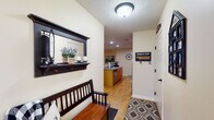 This single-floor home offers a thoughtfully designed layout that balances comfort and functionality throughout. The entryway sets a welcoming tone, featuring light wood-look flooring, a built-in wall shelf with mirror, and a bench — an organized and inviting introduction to the home. The kitchen is equipped with light wood cabinetry, laminate countertops, and a full suite of appliances, with hardwood-style flooring flowing seamlessly through the space. Adjacent to the kitchen, the dining area stands out with soaring vaulted ceilings, a striking arched window that frames outdoor views of open fields, and a sliding glass door that fills the room with natural light. The living room continues the vaulted ceiling design, anchored by a fireplace with a wall-mounted television above, and carpeted flooring that adds warmth throughout. Multiple bedrooms offer carpet flooring, natural light from windows with outdoor views, and ceiling fans for comfort. A shared full bathroom features dual sinks with wood cabinetry, a large mirror with overhead lighting, and hardwood-style flooring. Completing the home is a practical laundry room housing a full washer and dryer set alongside the home's mechanical systems, with overhead shelving for additional storage.