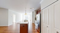 This single-floor residence is designed with an open, flowing layout that connects the kitchen and living areas seamlessly. The kitchen serves as a central feature, showcasing an elongated island topped with granite countertops and an integrated sink, illuminated by pendant lighting above. Rich, dark wood cabinetry reaches toward the ceiling, complemented by a tile backsplash and a full suite of stainless steel appliances, including a French door refrigerator, range, and microwave. Warm hardwood flooring runs throughout the main living areas, reflecting natural light that pours in through large sliding glass doors fitted with vertical blinds, opening to an outdoor view.

The living area is generously proportioned, with crown molding adding a refined architectural detail. Bedrooms feature plush carpeting and ample natural light through windows. One bedroom includes a set of double closet doors, while the primary suite connects to a well-appointed bathroom featuring a dual-sink vanity with granite countertops, dark cabinetry, tile flooring, a private water closet, and access to a spacious walk-in closet outfitted with wire shelving. The overall aesthetic is clean, neutral, and move-in ready.