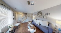 Located at 2920 Chapel Hill Road in Durham, NC, this two-story home offers a warm and inviting atmosphere with a farmhouse-inspired aesthetic carried throughout both levels. The main floor features rich hardwood flooring that flows through a bright living room, a dining area, and a functional kitchen. The living room is a welcoming gathering space accented by neutral gray walls, a decorative gallery wall, and large windows dressed with sheer curtains that allow natural light to fill the room. A carpeted staircase with white balusters connects the two floors with classic charm. The kitchen is well-appointed with white cabinetry, dark granite-style countertops, stainless steel appliances including a range, built-in microwave, and dishwasher, along with hardwood flooring that ties the space together. Upstairs, the spacious primary bedroom features plush carpet, a ceiling fan, a bright window with sheer curtains, and ample closet space. The second bedroom is equally comfortable, also with carpet and ceiling fan. Both bathrooms are finished in soft gray tones with white wainscoting accents — one featuring a tub/shower combo. With five closets and two hallways, storage is plentiful throughout this well-organized home.