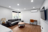 Located at 79 Duke Street in Hamilton, Ontario, this thoughtfully designed unit offers a smart and efficient use of space across a single floor. The open-concept main area features warm light wood flooring, crisp white walls, and recessed lighting that brightens the entire space. A wall-mounted mini-split unit provides climate control year-round. Corner windows invite natural light and offer views of the surrounding neighbourhood, creating an airy feel despite the compact footprint.

The spacious bedroom accommodates a full bed, nightstand, and wall-mounted TV, with recessed lighting and a grey entry door adding a modern touch. The living area is furnished with a grey sectional sofa, a round ottoman, and a dedicated desk and chair workspace — ideal for both relaxing and working from home.

The kitchen is a design highlight, featuring bold navy lower cabinetry, warm wood-toned upper cabinets, gold hardware, a white countertop, a stainless steel bottom-freezer refrigerator, and a matte black faucet over a stainless steel sink.

The bathroom is finished with floor-to-ceiling white textured tile, a sleek open walk-in shower with black framing, grey marble-style floor tiles, and matte black fixtures, delivering a clean, contemporary aesthetic throughout.