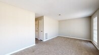 This single-floor residential unit offers a straightforward and functional layout designed to maximize livability. The living and dining areas are finished with wall-to-wall carpet in a neutral beige tone, complemented by clean white baseboards and soft, neutral-painted walls that create a calm, cohesive atmosphere throughout. Natural light filters into the carpeted bedroom through a window fitted with blinds, adding brightness to the space. An additional carpeted room connects seamlessly to the kitchen, providing a versatile dining or flex area. The kitchen is equipped with white upper and lower cabinetry, dark laminate countertops, a double-basin stainless steel sink, and black appliances including a coil-top electric range with overhead ventilation hood and a dishwasher. Wood-look vinyl flooring anchors the kitchen, offering a durable and easy-to-maintain surface. Closet space is provided with a built-in shelf and hanging rod, offering practical storage solutions. HVAC vents are present throughout, ensuring climate control across the unit. The overall design is clean, neutral, and move-in ready, suited for those seeking a no-frills, well-maintained living space.