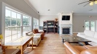 Located at 9400 Havenbrooke Way in Knoxville, Tennessee, this single-floor community space serves as a functional and inviting gathering hub. The open-concept layout seamlessly connects a fully equipped kitchen with a spacious living area, creating a versatile environment for socializing and relaxation.

The living room is anchored by a classic white-trimmed fireplace with a wall-mounted television above it, flanked by rich wood bookshelves and complemented by warm hardwood flooring. Crown molding and vaulted ceilings add architectural elegance, while large windows on the exterior wall flood the room with natural light and offer views of the surrounding greenery.

The kitchen features warm honey-toned cabinetry, dark granite countertops, tile flooring, and stainless steel appliances including a range, refrigerator, and dishwasher. French doors lead directly to an outdoor area, enhancing accessibility and airflow.

A standout feature of this space is the adjoining fitness center, visible through dramatic floor-to-ceiling glass panels. The gym is outfitted with a variety of cardio and strength equipment and is illuminated by striking geometric hexagonal LED lighting, giving it a modern, high-energy aesthetic. The transparent partition allows the fitness center to feel integrated with the main living area while maintaining a distinct, dedicated workout environment.