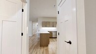 This single-story, 2-bedroom, 2-bathroom home offers a clean, modern aesthetic throughout, characterized by light wood-tone flooring, crisp white walls, and consistent use of warm natural tones. The open-plan kitchen and living area serves as the heart of the home, featuring a central island with white countertops, warm wood cabinetry with matte black hardware, and a full suite of stainless steel appliances including a range, over-the-range microwave, dishwasher, and French-door refrigerator. The entry foyer welcomes residents with natural light pouring in through flanking windows alongside a classic wood-paneled front door. The generously sized primary bedroom offers a comfortable, carpeted retreat, while the second bedroom also features carpet flooring, a ceiling fan, and a sliding-door closet. Both bedrooms receive natural light, with the second bedroom boasting a large picture window with outdoor views of surrounding greenery. The two bathrooms are finished with wood-tone vanities, white countertops, and light wood-style flooring. A dedicated laundry room accommodates a full-size washer and dryer with additional upper cabinetry for storage. Throughout the home, the cohesive design palette and thoughtful layout create a bright, functional, and inviting living environment.