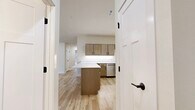 This single-story, 2-bedroom, 2-bathroom home offers a clean, modern aesthetic throughout, characterized by light wood-tone flooring, crisp white walls, and consistent use of warm natural tones. The open-plan kitchen and living area serves as the heart of the home, featuring a central island with white countertops, warm wood cabinetry with matte black hardware, and a full suite of stainless steel appliances including a range, over-the-range microwave, dishwasher, and French-door refrigerator. The entry foyer welcomes residents with natural light pouring in through flanking windows alongside a classic wood-paneled front door. The generously sized primary bedroom offers a comfortable, carpeted retreat, while the second bedroom also features carpet flooring, a ceiling fan, and a sliding-door closet. Both bedrooms receive natural light, with the second bedroom boasting a large picture window with outdoor views of surrounding greenery. The two bathrooms are finished with wood-tone vanities, white countertops, and light wood-style flooring. A dedicated laundry room accommodates a full-size washer and dryer with additional upper cabinetry for storage. Throughout the home, the cohesive design palette and thoughtful layout create a bright, functional, and inviting living environment.