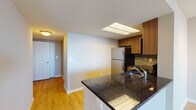 This single-floor residence offers a thoughtfully designed layout that balances functionality and comfort. The kitchen serves as a central highlight, featuring warm wood-toned cabinetry, dark granite countertops, a stone tile backsplash, and a full suite of stainless steel appliances including a refrigerator, microwave, and range. A skylight overhead floods the kitchen with natural light, while a peninsula with a built-in sink provides additional prep space and opens toward the living area. The living room is generously proportioned, finished with light hardwood-style flooring and track lighting on a textured ceiling. A full-width sliding glass door leads to an enclosed balcony, inviting abundant natural light into the space. A hallway connects the main living areas to the private rooms, including a carpeted bedroom with a large window fitted with vertical blinds. The bathroom is clean and functional, featuring a full soaking tub and shower combination with chrome fixtures. Throughout the unit, white trim, neutral wall tones, and consistent flooring choices create a cohesive, move-in-ready atmosphere.