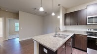 This single-floor Austin residence offers four bedrooms, two bathrooms, and a thoughtfully designed open-concept layout. The combined kitchen and living area serves as the heart of the home, where rich hardwood-style flooring extends throughout. The kitchen is well-appointed with dark espresso cabinetry, granite countertops, a subway tile backsplash, stainless steel appliances including a range and over-the-range microwave, and a peninsula with pendant lighting overhead—providing both additional prep space and a casual dining option.

The living area is generously proportioned, featuring a ceiling fan, neutral walls, and large windows with blinds that invite natural light and offer views of surrounding greenery. A sliding door provides direct outdoor access. The bedrooms are carpeted and comfortably sized, each with closet access. The bathrooms feature dark vanity cabinetry with light countertops and a tiled tub-shower combination. A dedicated laundry area accommodates a full-size washer and dryer with built-in shelving above. The overall aesthetic is modern and cohesive, with consistent neutral tones throughout.