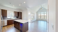 Located at 12890 S Black Bob Rd in Olathe, Kansas, this thoughtfully designed one-bedroom, one-bathroom unit combines contemporary finishes with an open, airy layout. Soaring vaulted ceilings elevate the open-concept kitchen and living area, creating a sense of spaciousness well beyond the unit's footprint. Large windows flood the living room with natural light and frame views of the surrounding community's landscaped grounds and gazebo.

The kitchen is a standout feature, showcasing rich dark walnut-toned cabinetry, a striking quartz-topped island with a built-in beverage cooler, grey tile backsplash, and a full suite of stainless steel appliances. Light hardwood flooring runs throughout the main living areas, complementing the clean, neutral palette.

The generously sized bedroom features plush carpeting, a ceiling fan, and its own window with community views. The full bathroom offers a double-sink vanity with quartz countertops, dark wood cabinetry, a glass-enclosed shower, and hardwood-style flooring. A private balcony extends the living space outdoors, offering elevated views of the well-maintained community grounds below.