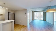 Located in the heart of downtown Montréal on Rue de Bleury, this two-bedroom, one-bathroom unit offers a modern urban living experience with a thoughtfully designed open layout. Light hardwood flooring flows throughout, complemented by exposed concrete ceilings that lend an industrial-contemporary character to the space.

The living area is anchored by expansive floor-to-ceiling windows and a glass door that frame impressive views of the Montréal skyline, filling the space with abundant natural light. The kitchen features white cabinetry, a subway tile backsplash, stainless steel appliances including a full-size refrigerator and built-in microwave, and a peninsula with a built-in sink — ideal for both cooking and casual dining.

Both bedrooms are well-proportioned and bright, each benefiting from large windows or glass doors that open to city views. The primary bedroom includes access to a dedicated closet, while a second closet provides additional storage. The exposed concrete ceiling detail carries through the bedrooms, maintaining a cohesive modern aesthetic.

The bathroom is finished with large-format tile and includes a walk-in shower. A stacked washer and dryer unit is conveniently integrated within the bathroom, adding practical in-unit laundry. This well-appointed unit combines contemporary finishes with striking urban views in one of Montréal's most central locations.