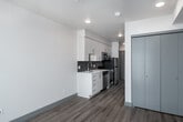 This contemporary single-floor unit is designed with clean lines and a modern aesthetic that carries throughout every room. The galley-style kitchen is efficiently laid out and well-appointed, featuring white flat-front cabinetry extending to the ceiling, light quartz countertops, a gray subway tile backsplash, a stainless steel undermount sink, and a full suite of stainless steel appliances including a gas range, microwave, dishwasher, and refrigerator. Generous cabinet storage ensures ample space for organization. The living area is bright and open, benefiting from large floor-to-ceiling sliding glass doors that lead directly to a private balcony, flooding the interior with natural light and offering outdoor views of the surrounding neighborhood. The bedroom is a calm, minimalist space with clean white walls, wood-look flooring, and a sliding door. A large built-in closet with sleek panel doors provides substantial storage. Throughout the unit, durable wood-look plank flooring in warm and cool tones creates a cohesive, contemporary look, while crisp white walls and recessed lighting contribute to a bright, airy ambiance. The overall design is practical yet polished, making the most of every inch of the space.
