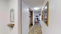 This single-story 1-bedroom, 1-bathroom residence offers a thoughtfully designed layout that balances functionality and comfort. The entryway leads into a hallway that sets the tone for the space, featuring warm-toned wood-look flooring that runs continuously throughout, creating a cohesive and inviting atmosphere.

A standout feature of the hallway is the built-in sliding-door closet, which provides generous storage capacity with integrated shelving and a hanging rod — ideal for organized, accessible storage. The sliding panel doors feature a clean, modern design that contributes to the streamlined aesthetic of the space.

The hallway opens into the bedroom, which is visible from the entry and appears well-proportioned, accommodating a full furniture arrangement including a bed, desk, and shelving. Framed wall art lines the hallway, adding a decorative touch that enhances the welcoming feel of the space.

Overhead, flush-mount ceiling lighting provides consistent illumination throughout. The textured ceiling and neutral white walls create a bright, clean backdrop that complements the natural wood-tone flooring. Overall, the unit presents a practical and comfortable living environment with attention to storage and design detail.