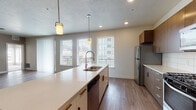 This well-designed single-floor residence offers a thoughtful layout that balances open communal spaces with comfortable private areas. The open-concept living and dining area is anchored by light hardwood-style flooring, a ceiling fan, and a generous bank of windows with views of the surrounding urban environment, flooding the space with natural light. Sliding glass doors lead to a private balcony, extending the living area outdoors.

The kitchen is a standout feature, showcasing warm wood-toned cabinetry, white quartz countertops, a subway tile backsplash, and a full suite of stainless steel appliances including a gas range, microwave, refrigerator, and dishwasher. A large central island with pendant lighting provides additional prep space and casual seating. In-unit laundry is also conveniently accessible from the kitchen area.

The bedrooms are carpeted and well-proportioned, each benefiting from multiple windows that invite natural light and urban views. Both bathrooms are finished with wood-toned vanity cabinetry, white countertops, hardwood-style flooring, and full shower-tub combinations with curved curtain rods. The neutral color palette and consistent finishes throughout create a cohesive, modern aesthetic.
