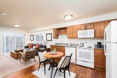 This single-floor residence in Covington, Washington, offers a thoughtfully designed layout that balances functionality and comfort. The kitchen serves as a practical centerpiece, featuring warm honey-toned wood cabinetry, a full suite of white appliances including a refrigerator, electric range, built-in microwave, and dishwasher, as well as generous counter space and ample storage. The kitchen flows seamlessly into the dining area, which accommodates a round wooden table — ideal for everyday meals. Adjacent to the dining space, the living room provides a welcoming retreat with neutral-toned walls, vertical blinds allowing natural light to filter in, and a sliding glass door that opens to an outdoor balcony. The bedroom is a calm and restful space, carpeted for comfort, with a large window fitted with vertical blinds, a baseboard heater, and room for a full-sized bed and furnishings. The bathroom features a wide vanity with a large mirror, warm wood cabinetry, and a shower-tub combination. Notably, in-unit laundry is conveniently situated within or adjacent to the bathroom. Hardwood-style flooring runs throughout the kitchen and dining areas, tying the space together with a cohesive, warm aesthetic throughout.