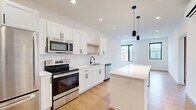 Located at 100 N Farwell St in Eau Claire, Wisconsin, this thoughtfully designed one-bedroom, one-bathroom unit offers a clean, modern aesthetic across a single floor. The open-concept kitchen and living area serves as the heart of the space, anchored by a sleek white island with a minimalist metal base and stylish pendant lighting above. The kitchen is outfitted with white shaker cabinetry featuring matte black hardware, a subway tile backsplash, stainless steel appliances including a refrigerator, range, microwave, and dishwasher, and a black-finish sink faucet. Light bamboo hardwood flooring extends throughout, complementing the bright white walls and recessed lighting for a warm, cohesive feel. Large windows in the living area invite natural light and offer views of the surrounding neighborhood. The bedroom is a comfortable, well-proportioned room featuring a sliding barn door, a wall-mounted mini-split unit, and a window overlooking the exterior. A dedicated closet with wire shelving provides organized storage. The bathroom is finished with large-format tile flooring, a wood-toned vanity with a white countertop, a wide mirror, and matte black fixtures, completing this contemporary and efficiently designed living space.