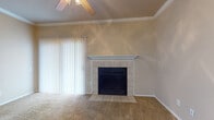 This single-story home offers a well-organized layout with distinct living spaces throughout. The living room serves as a central gathering area, highlighted by a tile-surround fireplace with a white mantel and a vaulted ceiling fitted with a ceiling fan. A sliding glass door with vertical blinds opens to an outdoor view, filling the space with natural light. Soft carpeting runs throughout the main living areas, contributing to a warm, comfortable atmosphere. Crown molding along the ceilings adds a polished architectural detail to the living and dining areas.

The dining area is a bright, defined space featuring a pendant light fixture and two windows dressed with horizontal blinds that allow generous natural light. The kitchen is equipped with warm wood-toned cabinetry, dark laminate countertops, a double stainless steel sink positioned beneath a window with an outdoor view, and a built-in dishwasher. The bathroom includes hardwood-style flooring, a tiled tub and shower combination with a decorative accent border, and a vanity with dark countertops that complement the overall design. The 3D scan reveals a compact, efficiently arranged floor plan with well-defined rooms throughout the home.