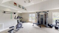 Located at 3220 Watchman Dr in Montgomery, AL, this fitness center is a thoughtfully designed single-floor facility offering a comprehensive workout environment. The space is organized into distinct functional zones, beginning with a welcoming entry foyer that features neutral gray walls, crown molding, carpeted tile flooring, and framed artwork, setting a clean and polished tone upon arrival.

The main exercise area is generously proportioned, accommodating a wide range of fitness equipment without feeling crowded. Cardio equipment includes an elliptical trainer and treadmill, positioned alongside a wall-mounted pull-up bar and a full-length mirror that enhances the sense of space. A multi-station cable machine serves as a focal point in the strength training section, complemented by a flat utility bench, a dedicated dumbbell and kettlebell rack, and medicine balls for functional training. Resistance bands and additional accessories are neatly organized on wall-mounted holders.

Vaulted ceilings in portions of the workout area add visual openness, while multiple windows along the perimeter allow abundant natural light to filter in. A ceiling fan provides added air circulation. The carpeted tile flooring throughout offers both comfort and durability, making this fitness center a practical and inviting space for a variety of training needs.
