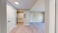 This single-floor residence offers a clean, neutral aesthetic throughout, characterized by light-toned walls, crisp white trim, and a consistent use of light wood-finish flooring across the main living areas. The open layout connects the main living space to the kitchen and entryway, creating a functional and cohesive flow.

The kitchen is a notable feature, equipped with white shaker-style cabinetry, marble-look stone countertops, and stainless steel appliances including an electric range and built-in microwave. A utility panel is conveniently accessible near the kitchen area, and a sink with white cabinetry is visible along the adjacent wall.

The living area benefits from a door that opens to an outdoor space, allowing natural light to filter in. A textured ceiling adds subtle architectural detail to this area.

The bedrooms are finished with plush carpeting, providing a comfortable contrast to the hard flooring elsewhere. Each bedroom includes a double-door closet offering ample storage. The bathroom features a full tub and shower surround, a toilet, and built-in open shelving for added convenience.

Overall, the space presents a well-maintained, move-in-ready environment with practical storage solutions and a cohesive neutral palette throughout.