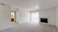 This single-floor residence presents a practical and well-organized layout with a neutral color palette of soft whites and beige tones throughout. The main living area is generously sized, featuring plush wall-to-wall carpeting, a textured popcorn ceiling, and a fireplace with a tiled surround and white mantel that serves as a focal point. Large windows fitted with horizontal blinds allow natural light to filter into the space, while a secondary room with vertical blinds provides additional outdoor views.

The kitchen is equipped with warm oak cabinetry, light-toned countertops, a coil-element range with over-the-range microwave, and a sink, with wood-look vinyl flooring tying the space together. Adjacent to the kitchen, a pass-through opening connects to the living area, enhancing the open feel of the layout.

The bedrooms are carpeted and well-lit, with multiple windows and ceiling fans providing comfort and ventilation. The bathroom includes a tiled tub-shower combination, a wood-vanity with a single sink and light countertop, a mirror, and wood-look flooring. The entry foyer features a ceiling fan and transitions from hard flooring to carpet, establishing a welcoming arrival point.