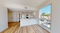 Located at 310 K St in Chula Vista, California, this single-floor unit showcases a clean, modern design with consistent light wood-tone flooring and crisp white walls throughout. The open-concept kitchen is a standout feature, anchored by a large peninsula with a white quartz countertop and an undermount sink. White shaker-style cabinetry lines the walls from floor to ceiling, complemented by stainless steel appliances including a gas range, over-the-range microwave, and a full-size refrigerator. A small clerestory window above the counter allows additional natural light into the kitchen. A large picture window adjacent to the living area frames outdoor views and fills the space with an abundance of natural light. The unit includes multiple well-proportioned bedrooms, each featuring the same warm wood-look flooring, neutral white walls, and windows that invite natural light. The primary bathroom offers a clean, well-appointed vanity with a white quartz countertop, under-cabinet storage, and a large mirror. A separate half bath includes a wall-mounted pedestal sink, mirror, and toilet. Recessed lighting throughout the unit adds to its bright, contemporary ambiance, and a built-in open shelving unit near the entry provides convenient storage.