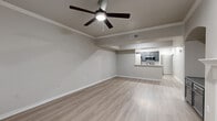 This single-story home offers a thoughtfully designed layout across a comfortable footprint, with light-toned luxury vinyl plank flooring and neutral gray walls throughout that create a cohesive, modern aesthetic. Crown molding and ceiling fans with integrated lighting are consistent features, adding architectural detail to the living spaces.

The open-concept living room serves as the heart of the home, highlighted by a wood-burning fireplace with a white mantel and blue-gray tile surround, a ceiling fan, and a window providing natural light and outdoor views. The space flows seamlessly into the kitchen, which is separated by a peninsula breakfast bar with a white countertop. The kitchen features gray cabinetry, a stainless steel appliance suite including a microwave, range, and refrigerator, a tile backsplash, and recessed and track lighting overhead.

A hallway connects the kitchen to the two bedrooms, bathroom, closet, and laundry area. The spacious primary bedroom includes a ceiling fan, crown molding, and access to a dedicated closet. The bathroom features a dual-sink vanity with dark cabinetry, white countertops, a large mirror, and a separate toilet compartment. The attached garage provides additional storage and parking capacity with an automatic opener.