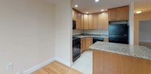 This single-floor residence offers a thoughtfully designed layout with warm hardwood flooring extending throughout the living spaces and bedrooms, creating a cohesive and inviting atmosphere. The open-concept living and dining area is generously sized, bathed in natural light from multiple windows that overlook lush greenery, and equipped with baseboard heating and wall-unit air conditioning for year-round comfort.

The kitchen is a functional and stylish centerpiece, featuring warm-toned wood cabinetry, granite countertops, black appliances including a gas range, microwave, refrigerator, and dishwasher, along with a central island that provides additional prep space. Recessed lighting illuminates the kitchen, enhancing its polished finish.

The bedrooms are well-proportioned, with one featuring a sliding double-door closet with built-in shelving, offering ample storage. Both rooms benefit from natural light and direct access to adjacent areas of the home.

The two bathrooms are finished with neutral tile flooring and tile wainscoting. One bathroom includes a granite-topped vanity with a white cabinet base and a glass-enclosed shower, while the other features a similarly elegant vanity and a glass shower enclosure, both conveying a clean and refined aesthetic throughout.