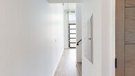 Located at 3279 San Marino St, Unit 402, in Los Angeles, CA, this two-level unit offers a thoughtfully designed layout spread across two floors. Light wood-tone luxury vinyl flooring runs consistently throughout, lending warmth and visual continuity to the entire space.

The main floor houses the kitchen and hallway areas. The kitchen is outfitted with modern flat-front cabinetry in a warm wood finish, stainless steel appliances including a gas range, over-the-range microwave, and a full-size refrigerator, complemented by clean white countertops and a sleek matte black sink faucet. The open layout adjacent to the kitchen provides a versatile living area with tall ceilings that enhance the sense of volume and openness.

A staircase leads to the upper level, which features a secondary hallway area bathed in natural light from a horizontal window that runs along the wall — a standout architectural detail that brightens the space. This upper level also provides direct access to the bathroom.

The bathroom is clean and minimalist in design, featuring a wall-mounted rectangular sink, a modern black-framed mirror with a built-in shelf, and light wood flooring that carries through from the rest of the unit. The crisp white walls throughout both floors contribute to a bright, airy ambiance, making the overall space feel open and contemporary.