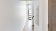 Located at 3279 San Marino St, Unit 402, in Los Angeles, CA, this two-level unit offers a thoughtfully designed layout spread across two floors. Light wood-tone luxury vinyl flooring runs consistently throughout, lending warmth and visual continuity to the entire space.

The main floor houses the kitchen and hallway areas. The kitchen is outfitted with modern flat-front cabinetry in a warm wood finish, stainless steel appliances including a gas range, over-the-range microwave, and a full-size refrigerator, complemented by clean white countertops and a sleek matte black sink faucet. The open layout adjacent to the kitchen provides a versatile living area with tall ceilings that enhance the sense of volume and openness.

A staircase leads to the upper level, which features a secondary hallway area bathed in natural light from a horizontal window that runs along the wall — a standout architectural detail that brightens the space. This upper level also provides direct access to the bathroom.

The bathroom is clean and minimalist in design, featuring a wall-mounted rectangular sink, a modern black-framed mirror with a built-in shelf, and light wood flooring that carries through from the rest of the unit. The crisp white walls throughout both floors contribute to a bright, airy ambiance, making the overall space feel open and contemporary.