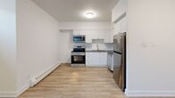 Located at 301–341 Traynor Ave in Kitchener, Ontario, this efficiently designed single-floor unit offers a clean, modern aesthetic throughout. Light wood-look laminate flooring runs seamlessly across the entire space, complemented by crisp white walls and a textured ceiling that together create a bright, cohesive interior.

The kitchen is a standout feature, outfitted with white shaker-style cabinetry, a classic subway tile backsplash, and a full suite of stainless steel appliances including a refrigerator, stove, built-in microwave, and dishwasher. A single-basin sink with a contemporary faucet completes the functional layout, making the kitchen both practical and visually appealing.

The open living area is well-proportioned, offering flexible space for various furniture arrangements. Horizontal transom-style windows positioned near the ceiling allow natural light to filter in, brightening the interior. Baseboard heaters are installed throughout, ensuring reliable warmth during cooler months.

A well-placed entryway provides a clear transition into the unit, with a closet nearby for convenient storage. The layout flows logically from the entrance through to the living and kitchen areas, maximizing the use of the available space. Overall, this unit presents a clean, updated environment suited for practical, day-to-day living.