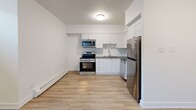 Located at 301–341 Traynor Ave in Kitchener, Ontario, this efficiently designed single-floor unit offers a clean, modern aesthetic throughout. Light wood-look laminate flooring runs seamlessly across the entire space, complemented by crisp white walls and a textured ceiling that together create a bright, cohesive interior.

The kitchen is a standout feature, outfitted with white shaker-style cabinetry, a classic subway tile backsplash, and a full suite of stainless steel appliances including a refrigerator, stove, built-in microwave, and dishwasher. A single-basin sink with a contemporary faucet completes the functional layout, making the kitchen both practical and visually appealing.

The open living area is well-proportioned, offering flexible space for various furniture arrangements. Horizontal transom-style windows positioned near the ceiling allow natural light to filter in, brightening the interior. Baseboard heaters are installed throughout, ensuring reliable warmth during cooler months.

A well-placed entryway provides a clear transition into the unit, with a closet nearby for convenient storage. The layout flows logically from the entrance through to the living and kitchen areas, maximizing the use of the available space. Overall, this unit presents a clean, updated environment suited for practical, day-to-day living.