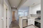 Located at 8320 Colesville Rd in Silver Spring, MD, this well-appointed one-bedroom, one-bathroom residence offers a thoughtfully designed layout across a single floor. The open-concept living and dining area is bright and airy, featuring light wood-tone flooring, neutral gray walls, ceiling fans, and multiple windows that bring in generous natural light. A decorative stacked-stone accent wall adds a distinctive architectural touch between the kitchen and living space. The kitchen is a standout, equipped with white shaker cabinetry, granite-style countertops, a gray subway tile backsplash, and a full suite of stainless steel appliances including a gas range, over-the-range microwave, dishwasher, and refrigerator. A peninsula with a sink offers additional prep space and casual seating. The bedroom is carpeted and spacious, featuring a ceiling fan, French doors providing natural light and outdoor access, and direct access to a closet. The bathroom is finished with marble-style tiled walls surrounding the soaking tub and shower, a white vanity with granite-style counters, and tile flooring. Five closets throughout provide exceptional storage. A dedicated hallway connects the rooms efficiently, completing this well-organized residence.