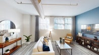 Located on W Court St in the heart of Indianapolis, this single-floor unit blends urban industrial character with contemporary finishes throughout. The living area is a standout space, featuring exposed spiral ductwork along white ceilings that adds an industrial edge. Large multi-pane windows line the walls, flooding the room with natural light and offering views of the surrounding cityscape. Light wood-style flooring runs throughout the main living areas, complementing a neutral palette accented by bold navy and steel-blue tones on select walls.

The kitchen is well-appointed with white cabinetry, granite countertops, stainless steel appliances, and a peninsula with bar seating beneath a sculptural chandelier. A mirrored backsplash detail above the cabinetry adds depth to the space.

The bedrooms are carpeted for comfort and feature the same bold blue accent walls, creating a cohesive design language. Each bedroom is generously proportioned with room for substantial furniture. Both bathrooms are finished with tile-surround tub-shower combinations, granite-topped vanities, and wood-look flooring, delivering a clean, polished aesthetic throughout.