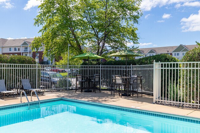 Acogedora zona de piscina al aire libre con tumbonas y mesas a la sombra, rodeada de exuberante vegetación y apartamentos modernos. - Avana Maple Grove