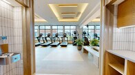 Located at 901 Third Ave N in Nashville, TN, this upscale fitness center offers a generously sized, single-floor layout designed to accommodate a full range of workout experiences. The space is defined by a refined modern aesthetic, featuring coffered ceilings with warm LED cove lighting that creates an inviting yet energizing atmosphere throughout.

The main gym floor is expansive, housing a comprehensive cardio zone lined with treadmills, stationary bikes, ellipticals, and rowing machines positioned along floor-to-ceiling windows that flood the space with natural light and offer views of the surrounding Nashville cityscape. A dedicated strength training area features cable machines, power racks, adjustable benches, dumbbells, kettlebells, and medicine balls, providing a complete free-weight and machine training environment.

A separate, dedicated group fitness and studio room features warm hardwood flooring, full-length mirrors along one wall, a large display screen, integrated speakers, and high clerestory windows that bring in additional daylight — ideal for yoga, stretching, or instructor-led classes.

Throughout the facility, light wood accents, potted greenery, and neutral flooring contribute to a clean, welcoming environment. The entrance is marked with a branded Starling welcome mat, setting a polished tone from the moment of arrival.