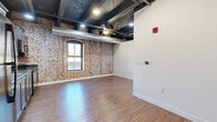 Located at 254 N Santa Fe Ave in Salina, Kansas, this one-bedroom, one-bathroom urban loft blends industrial character with modern finishes. The open-concept main living area combines the living room, dining space, and kitchen into one cohesive layout, making efficient use of the thoughtfully designed floor plan. Exposed red brick walls serve as a defining architectural feature throughout, complemented by dramatic dark-painted ceilings with visible ductwork and wood beam accents that lend an authentic loft aesthetic. Warm hardwood-style flooring runs continuously throughout the space, adding richness and cohesion. A ceiling fan and recessed lighting provide both comfort and illumination, while arched and framed windows invite natural light and offer views of the surrounding downtown streetscape. The kitchen is well-appointed with dark stained cabinetry, dark countertops, a subway tile backsplash, and black appliances including a refrigerator, range, dishwasher, and over-range microwave. The bedroom offers a comfortable and private retreat, with access to a dedicated closet. The bathroom features a dark wood vanity with a dark countertop, an undermount sink, and a large mirror with overhead lighting. Clean white walls in the bedroom and bathroom provide a balanced contrast to the industrial character found throughout the rest of the space.