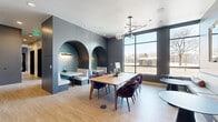 Located at 2287 Welton St in Denver's Five Points neighborhood, this thoughtfully designed single-floor commercial space offers a sophisticated blend of collaborative and private work environments. The layout comprises four distinct areas, each contributing to a cohesive, contemporary aesthetic defined by clean lines, mixed materials, and carefully curated furnishings.

The main lounge and gathering area serves as the centerpiece of the space, featuring light hardwood flooring, dark slate-toned wall panels, and a striking feature wall with two arched booth alcoves. Each alcove is finished with textured teal wallcovering, white bench seating, and dedicated wall-mounted lighting, creating intimate nooks ideal for focused work or casual meetings. A sculptural sputnik chandelier with globe pendants anchors the room, which also accommodates a central wood communal table with richly upholstered velvet chairs and additional seating along the perimeter.

Floor-to-ceiling windows flood the space with natural light and offer views of the surrounding streetscape. A glass-enclosed private office provides visual transparency while maintaining acoustic separation. Additional enclosed offices feature large windows and exposed concrete elements. A connecting corridor with hardwood floors ties the rooms together, while a tiled entry area with black metal railings completes the functional flow throughout.